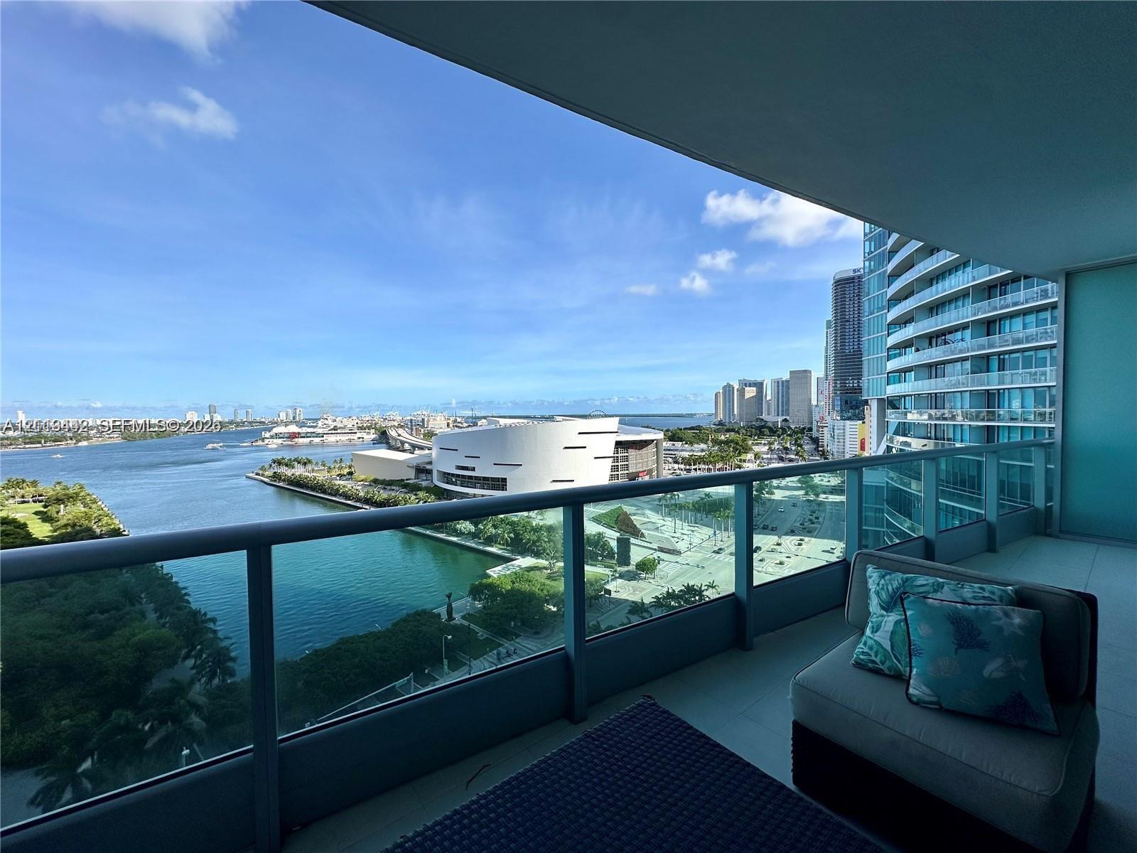 Covered balcony with a glass-panel railing, tile flooring, and expansive water and skyline scenery