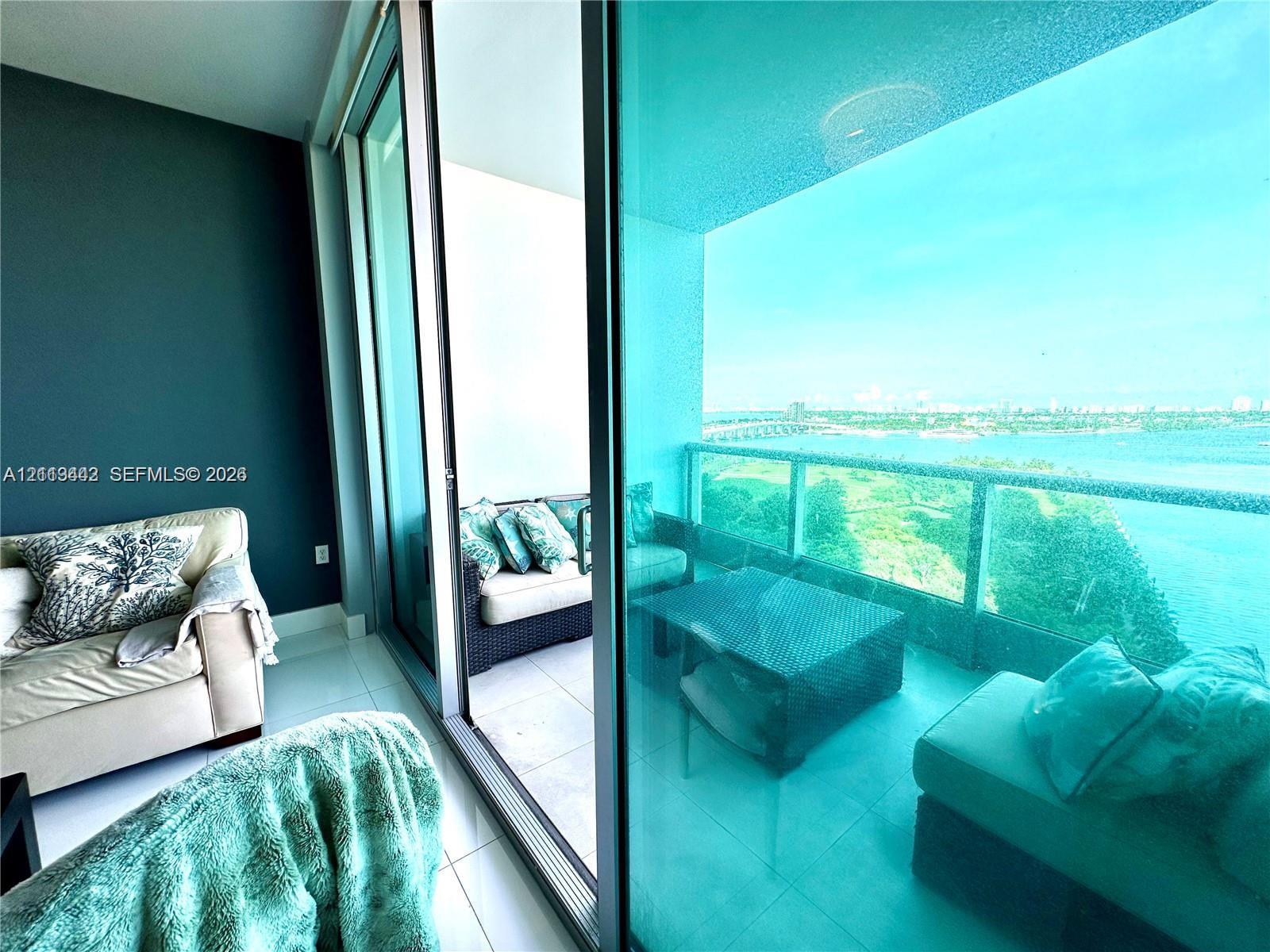 Full-height sliding glass doors opening to a private balcony with glass-panel railings and water scenery