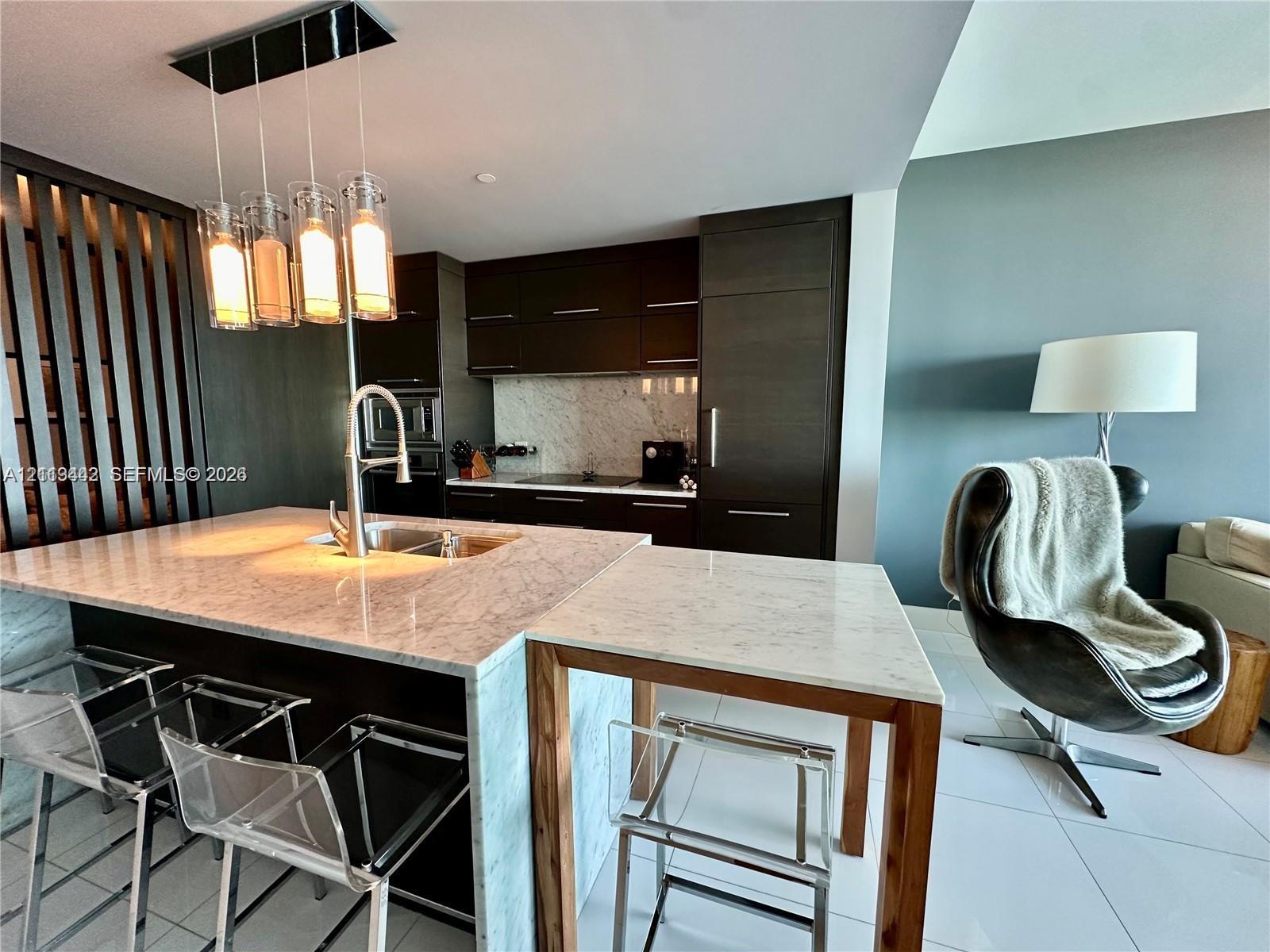 Kitchen featuring dark cabinetry, stone countertops with a waterfall edge, a built-in cooktop, integrated refrigeration, and a multi-light pendant fixture