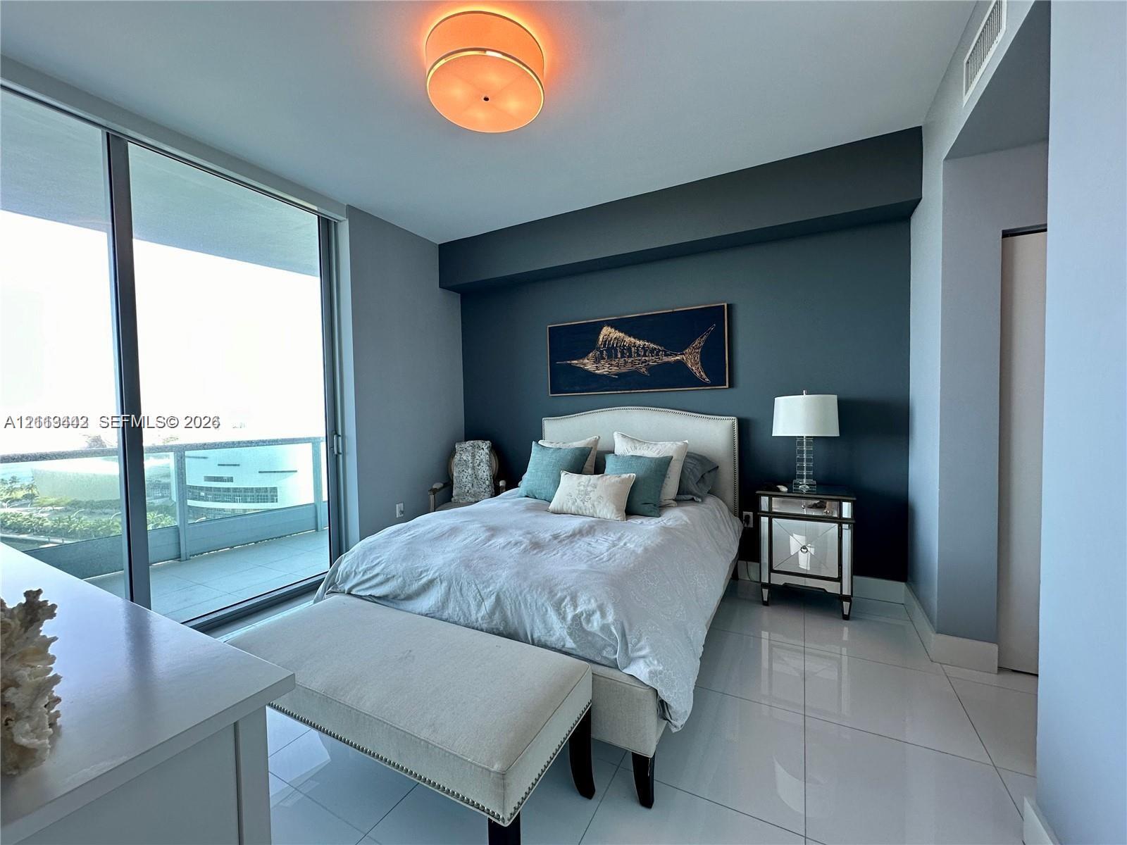 Floor-to-ceiling glass sliding doors opening to a balcony, polished tile flooring, accent wall, and circular semi-flush mount ceiling lighting