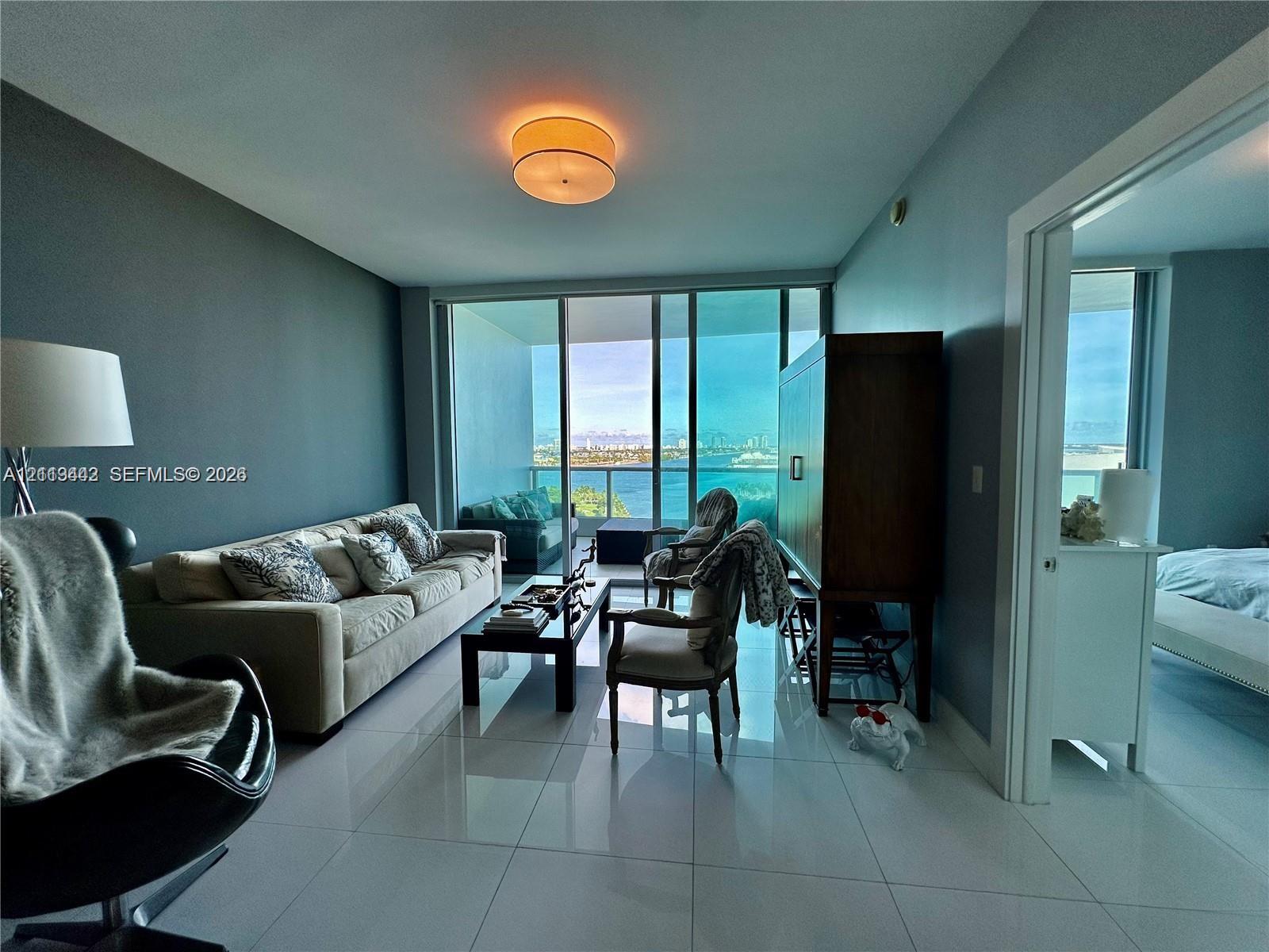 Floor-to-ceiling glass sliding doors, polished tile flooring, flush-mount drum lighting, and expansive water scenery