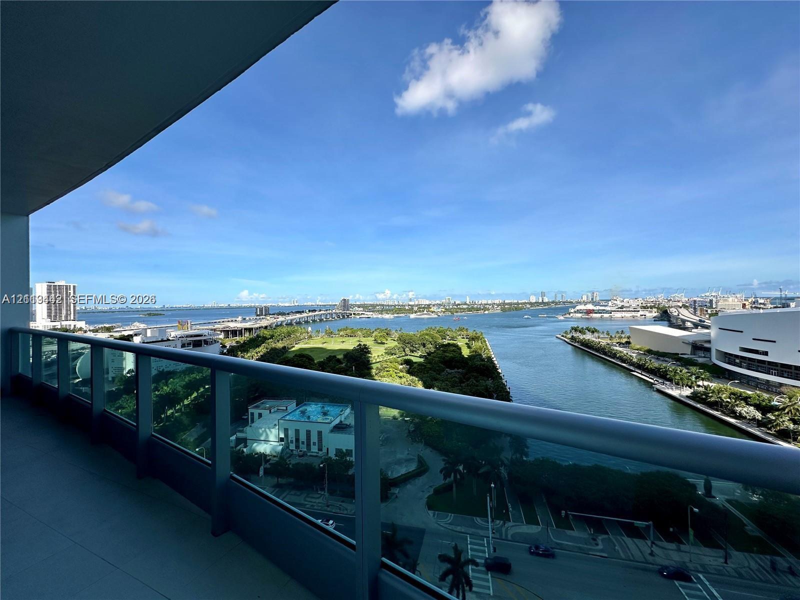 Covered balcony with a glass and metal railing overlooking the waterfront and cityscape