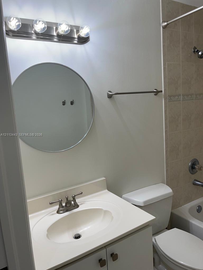 Bathroom featuring a round mirror, four-bulb vanity light fixture, vanity with an integrated sink, and a tiled shower surround