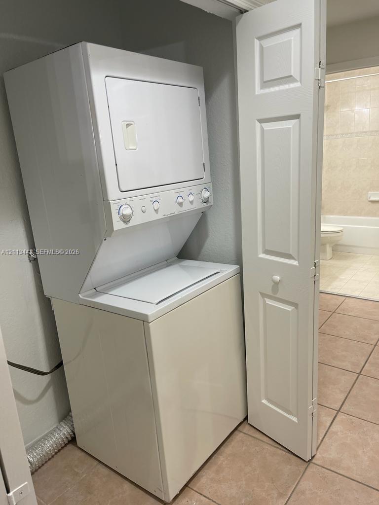 Stackable white top-load washer and dryer unit with white bi-fold closet door and tile flooring