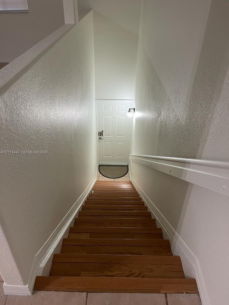 Staircase featuring wood-finish treads, a white wall-mounted handrail, and high-contrast paint finishes, leading to a panel-style entry door