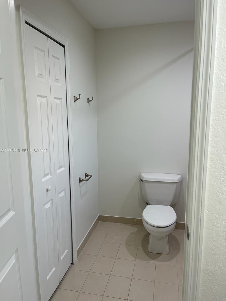Neutral-toned interior space featuring light-colored tile flooring, white bi-fold closet doors, a porcelain toilet, and wall-mounted brushed nickel hardware