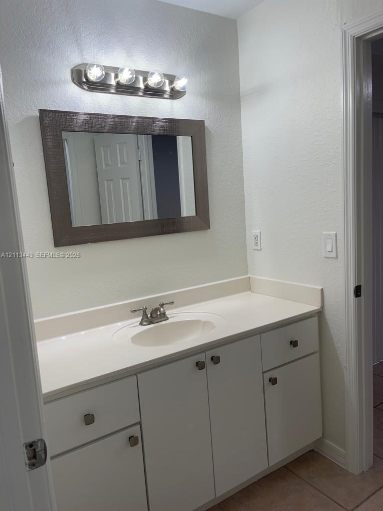 Bathroom vanity featuring white cabinetry, a solid-surface countertop with an integrated oval sink, chrome dual-handle faucet, framed wall mirror, and a four-bulb vanity light fixture