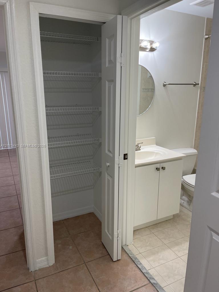 Built-in closet featuring white wire shelving, vanity with integrated basin, polished metal hardware, and ceramic tile flooring