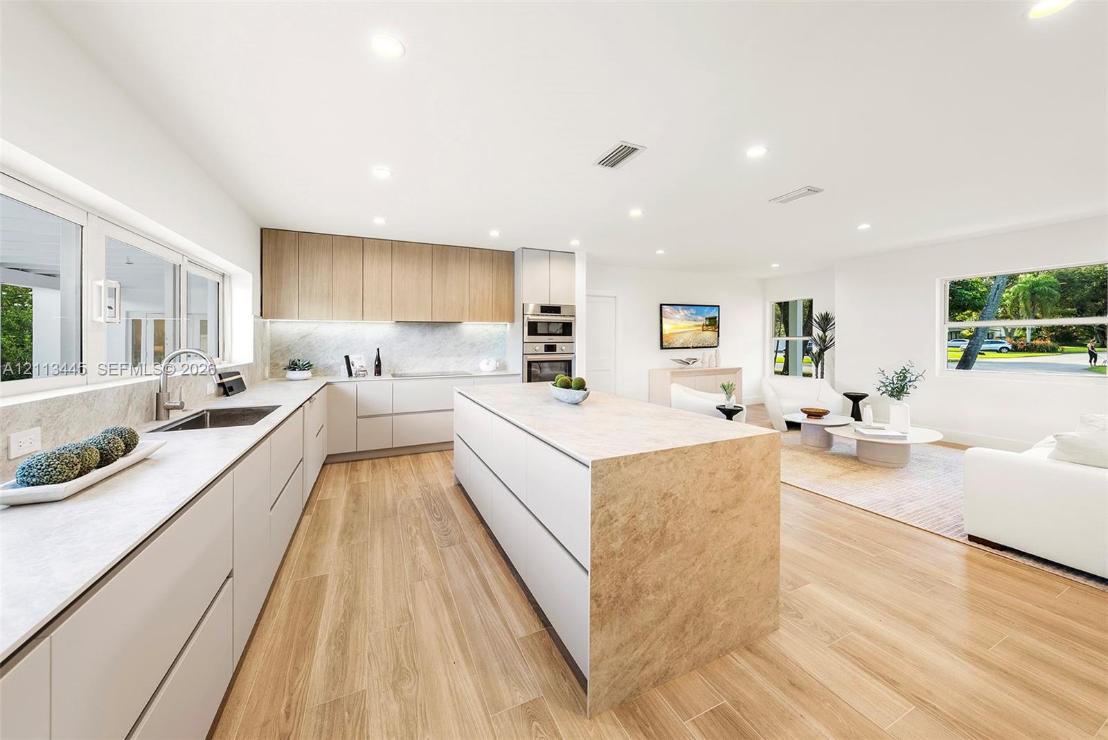 Kitchen featuring flat-panel cabinetry, a central island with stone-finish surfaces, integrated stainless steel double wall ovens, recessed lighting, and wood-finish flooring