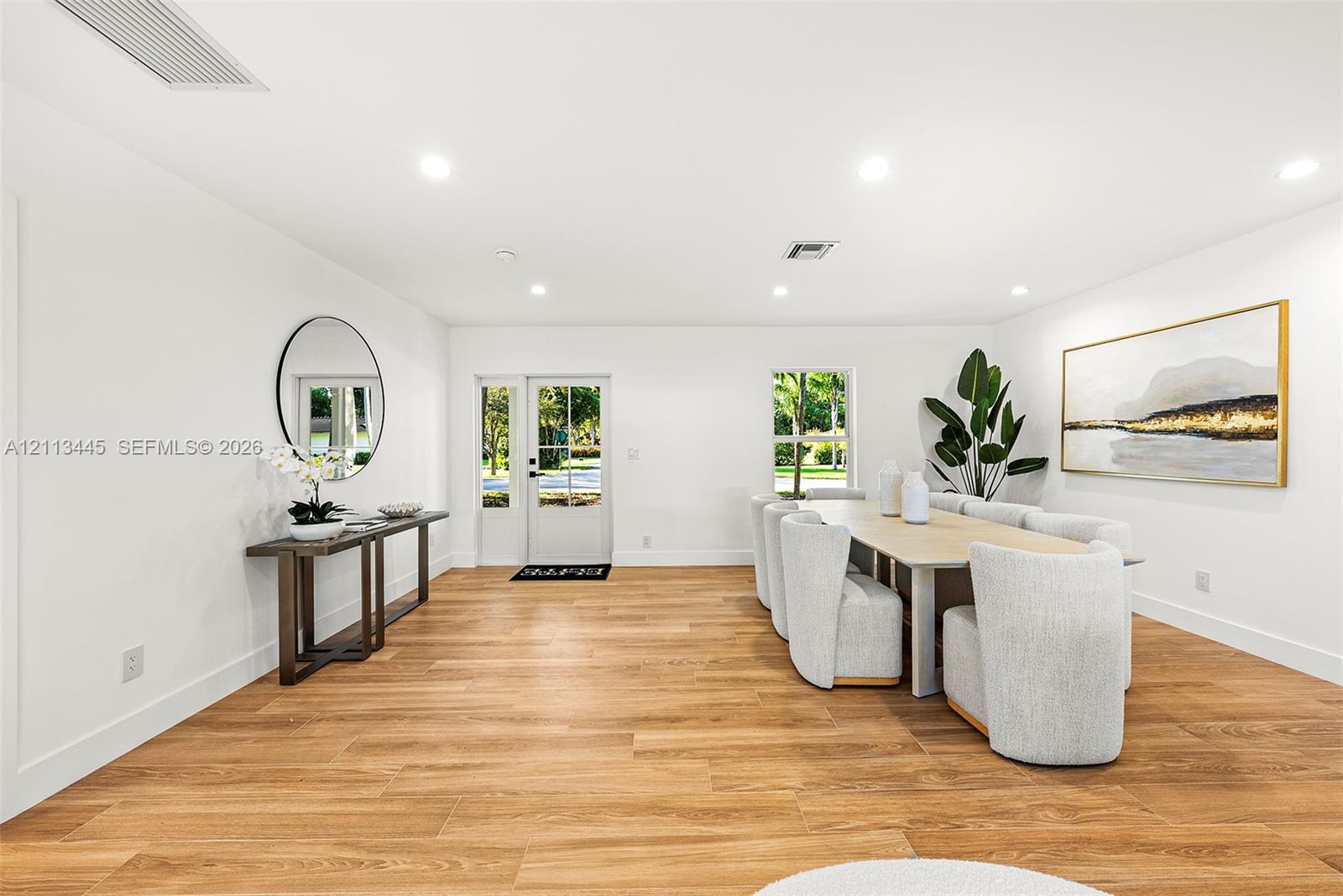 Open interior featuring wood-finish flooring, recessed lighting, and a white-framed glass paneled entry door Open interior featuring wood-finish flooring, recessed lighting, and a white-framed glass paneled entry door