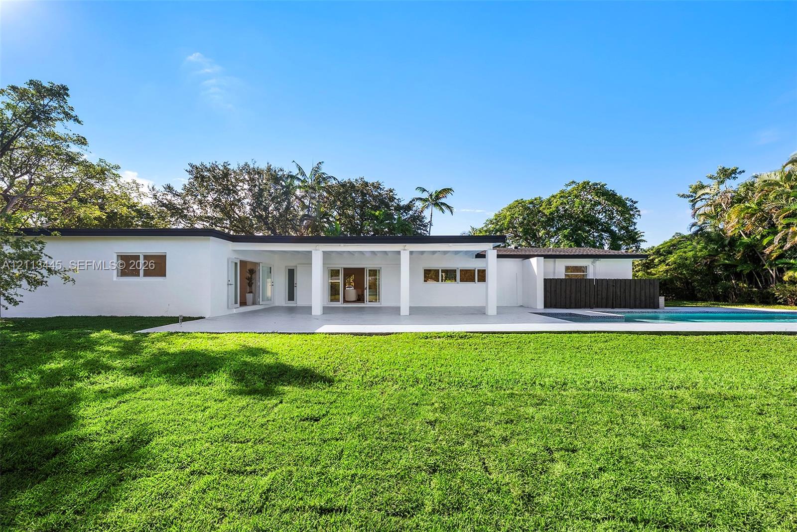 Mid-century modern architectural style featuring an expansive covered patio, white exterior finish, flat roofline, and swimming pool