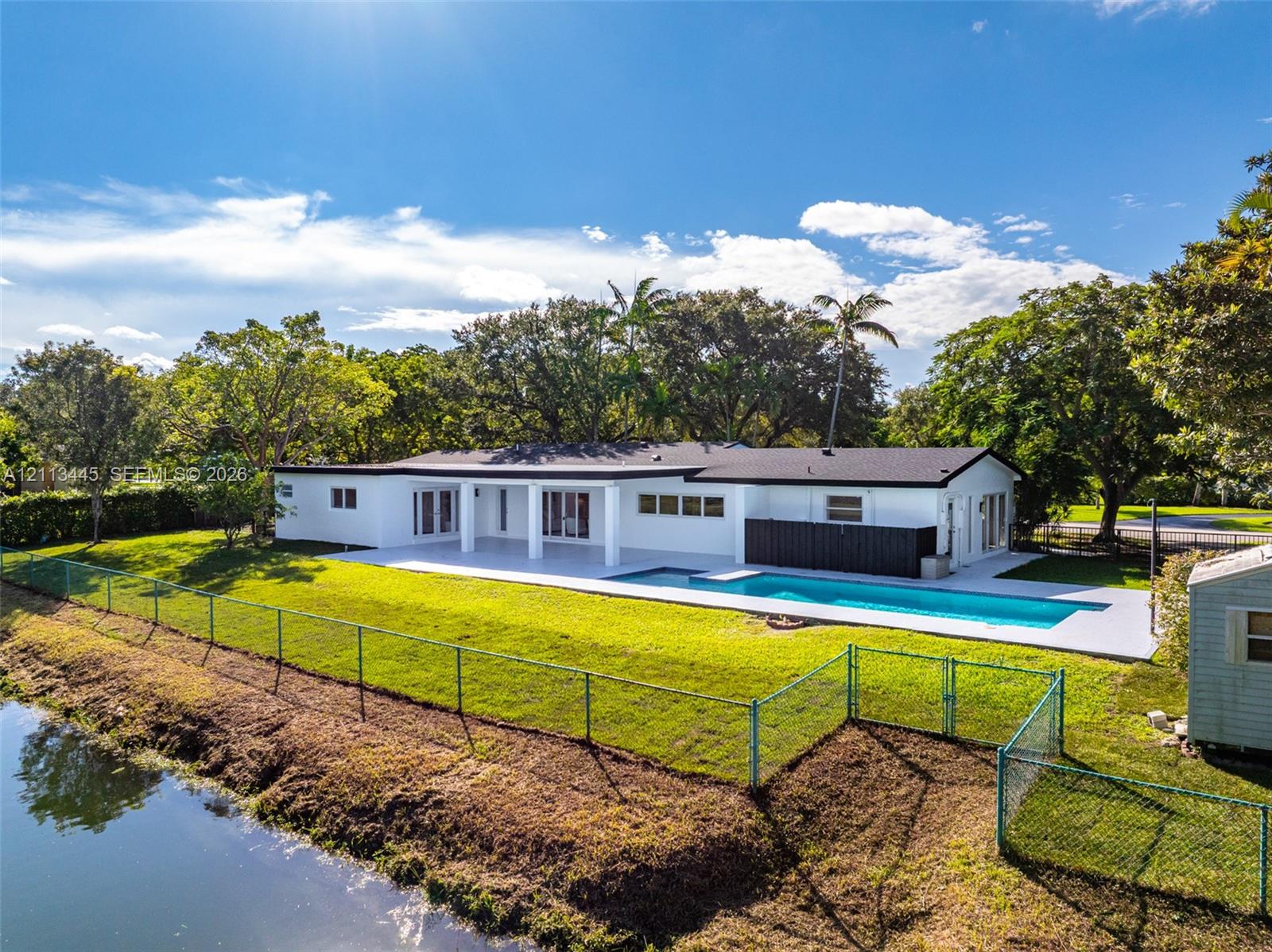 Single-story residence featuring a white exterior, expansive concrete patio, inground swimming pool, and water frontage