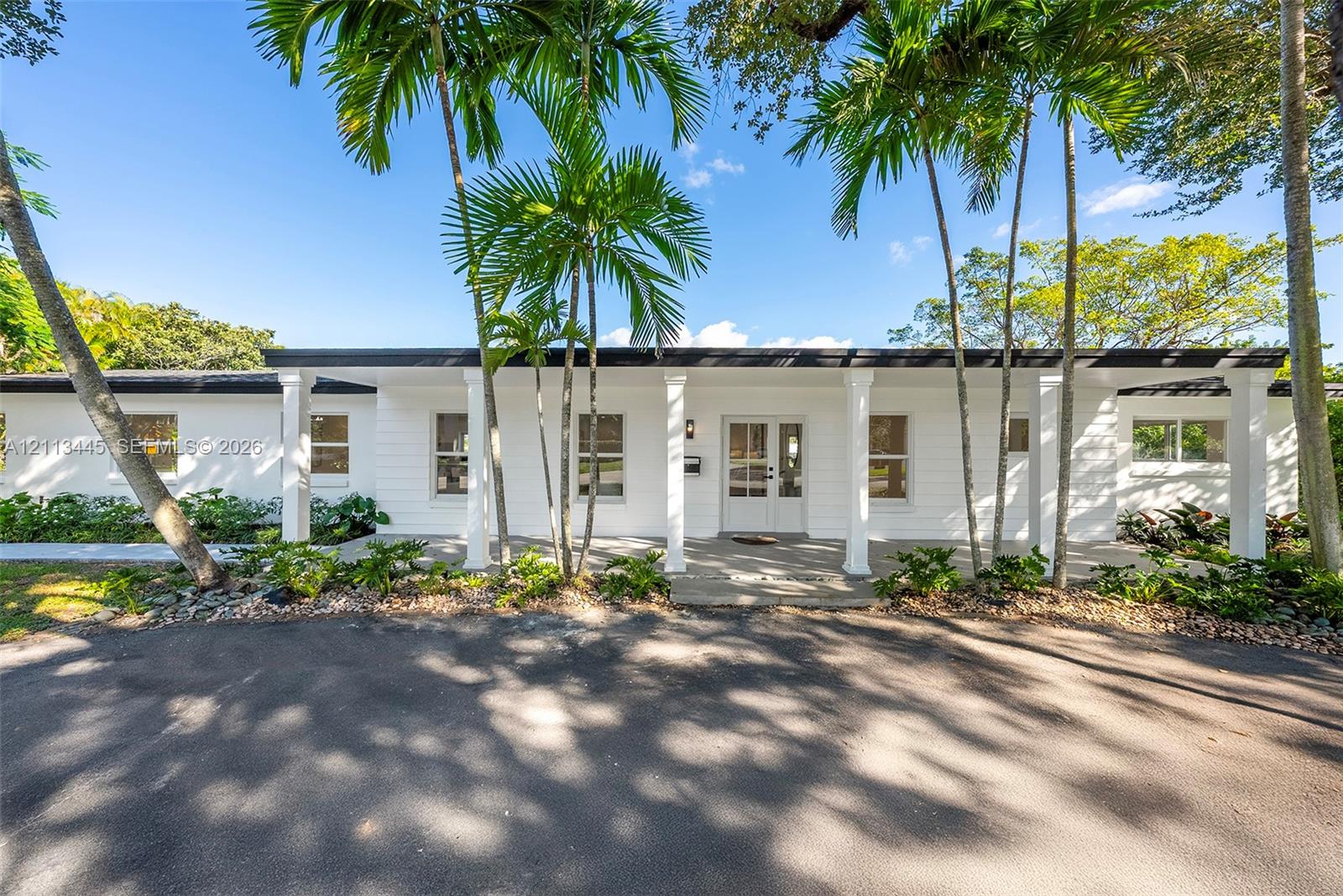 Single-story exterior featuring white horizontal siding, a covered entryway with square columns, double glass-paneled front doors, and established palm landscaping Single-story exterior featuring white horizontal siding, a covered entryway with square columns, double glass-paneled front doors, and established palm landscaping