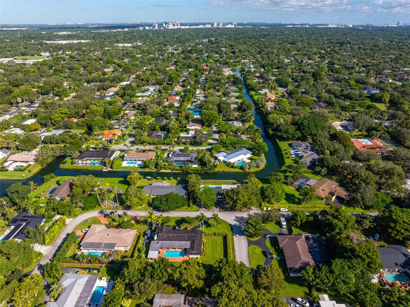 Aerial perspective featuring residential lots with canal frontage, mature trees, and dense foliage within a suburban setting