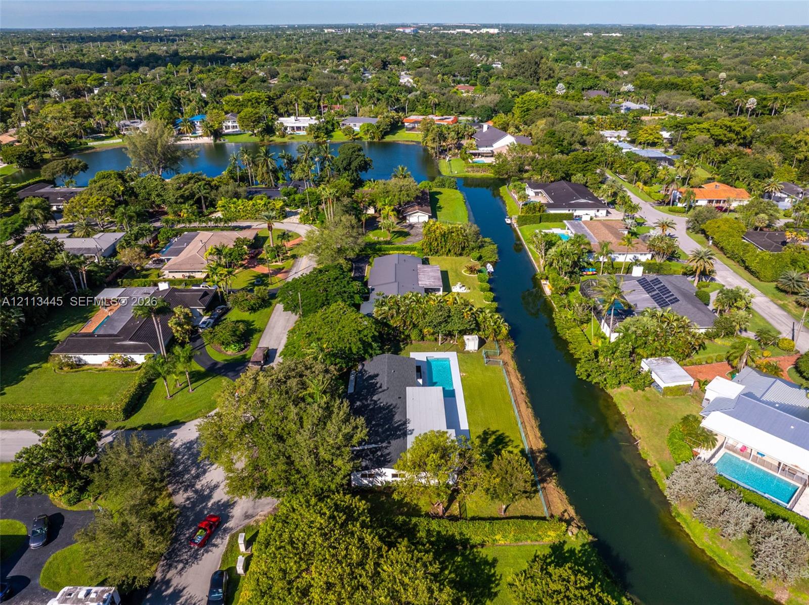 Aerial perspective of a waterfront property featuring a private swimming pool, a rectangular paved patio, expansive lawn, and direct canal access