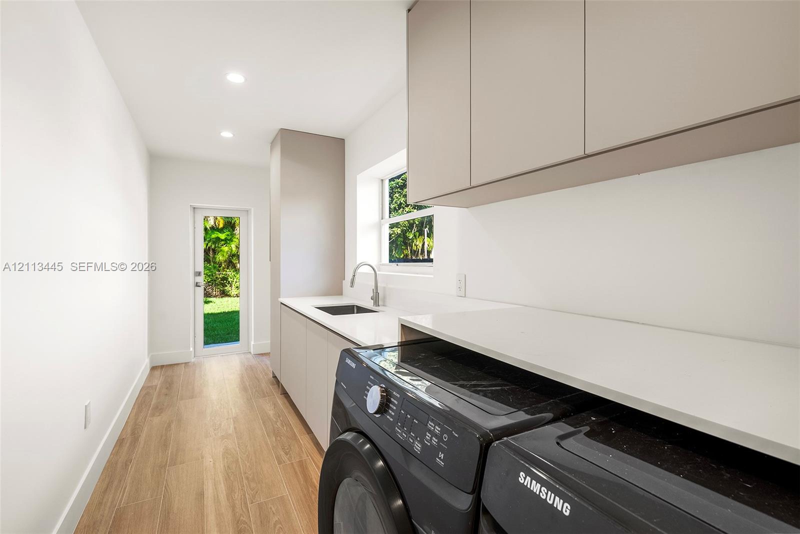 Utility area featuring flat-panel cabinetry, light-toned stone-finish countertops, an undermount sink with a gooseneck faucet, and wood-finish flooring
