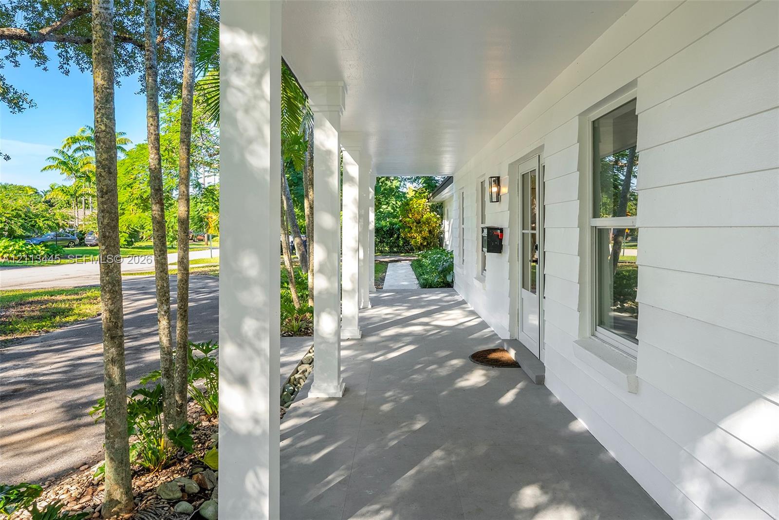 Covered front porch featuring white horizontal lap siding, square support columns, and a glass-paneled entry door