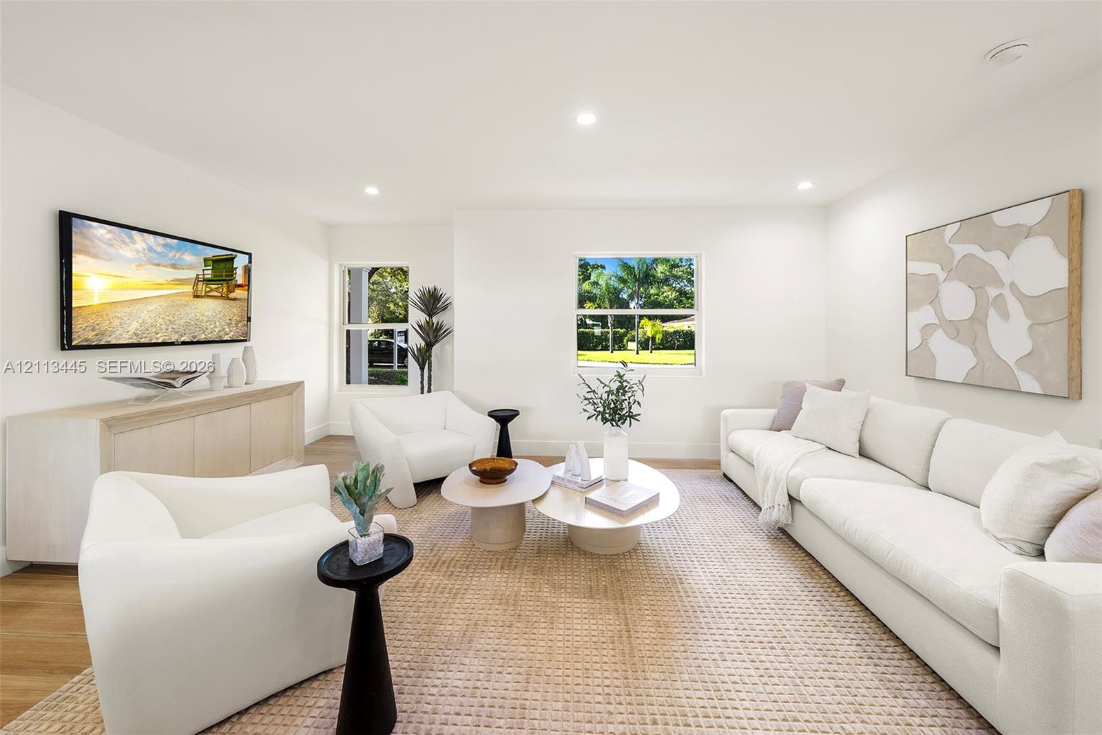 Neutral-toned interior space featuring light wood-finish flooring, recessed lighting, and multiple windows providing natural illumination
