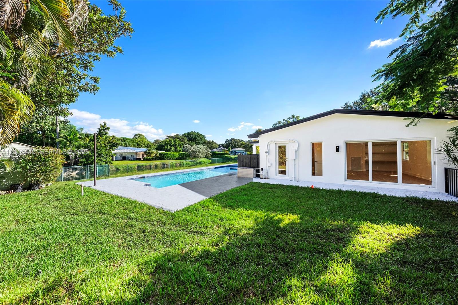 Backyard featuring an inground swimming pool, concrete pool deck, white stucco exterior, sliding glass doors, and manicured lawn