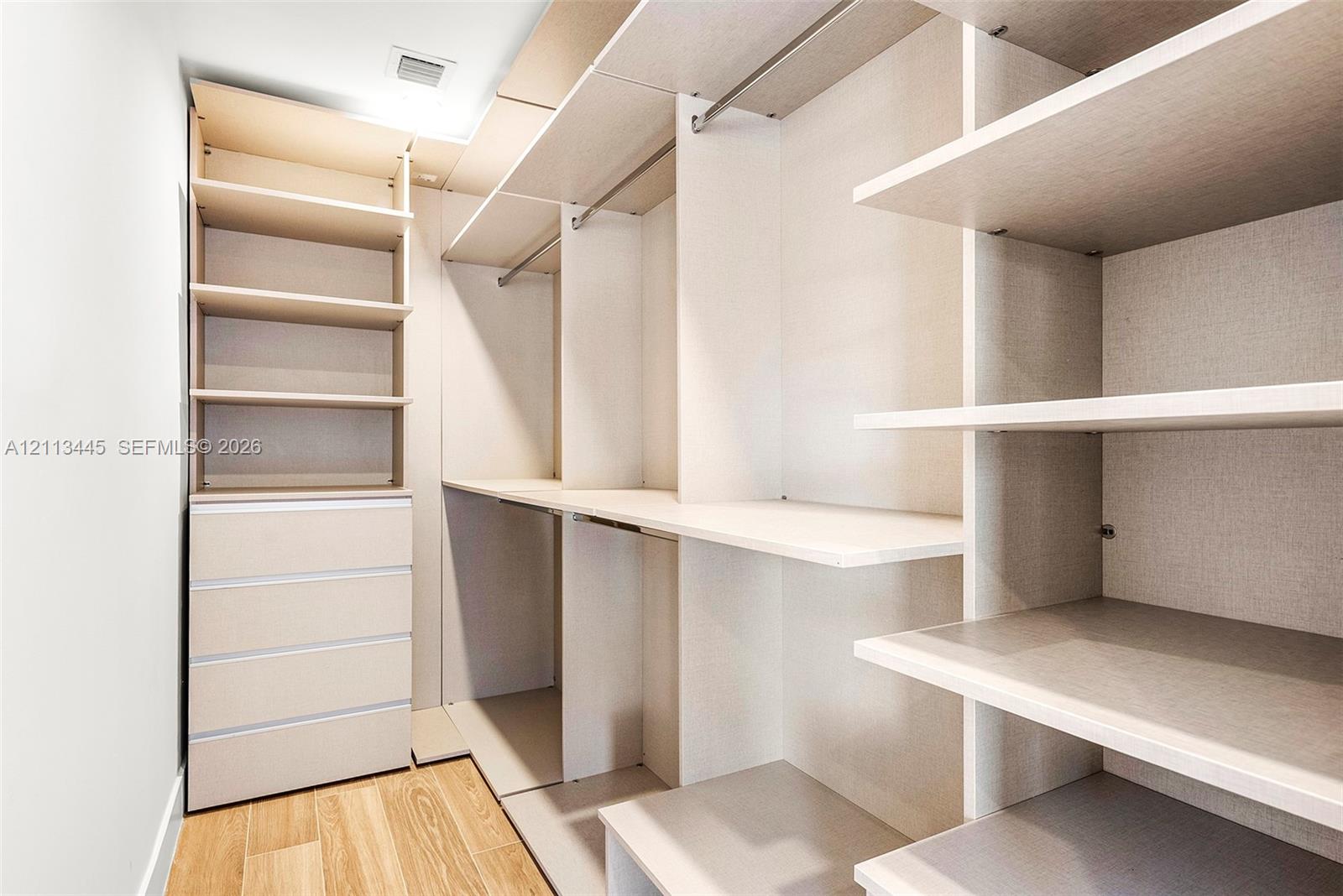 Walk-in closet featuring custom built-in cabinetry, integrated shelving, multi-level hanging rods, a four-drawer dresser unit, and wood-finish flooring