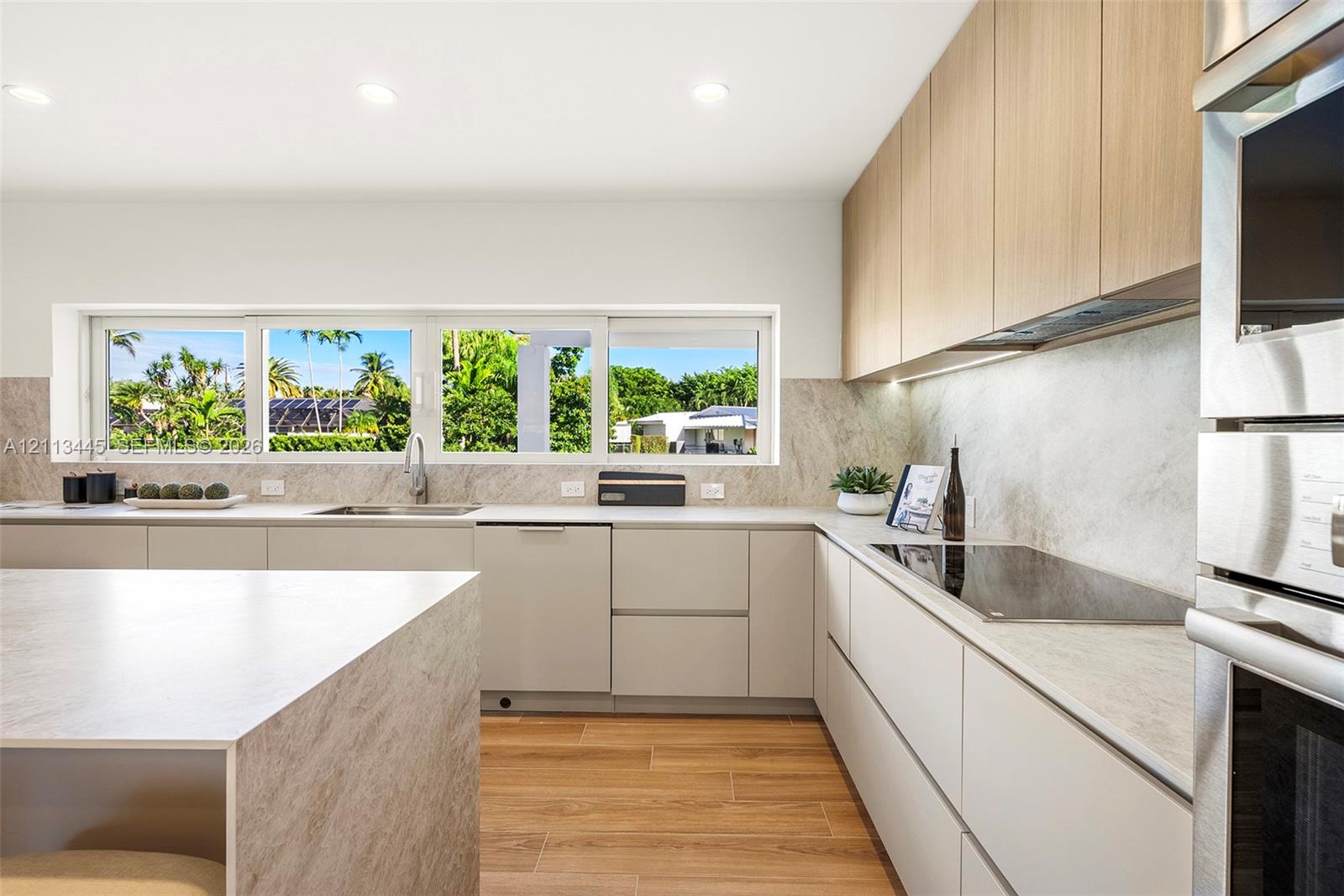 Kitchen featuring flat-panel cabinetry, wood-finish flooring, stone-finish countertops and backsplash, integrated stainless steel appliances, and a horizontal window
