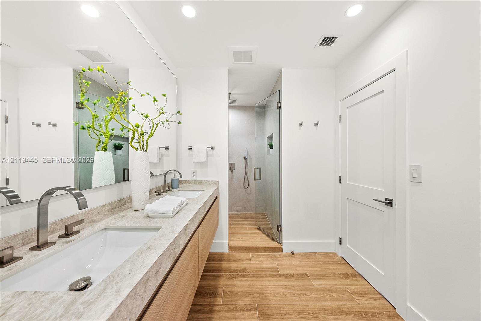Floating dual-sink vanity with stone-finish countertop, wood-finish cabinetry, frameless glass walk-in shower, and wood-finish flooring