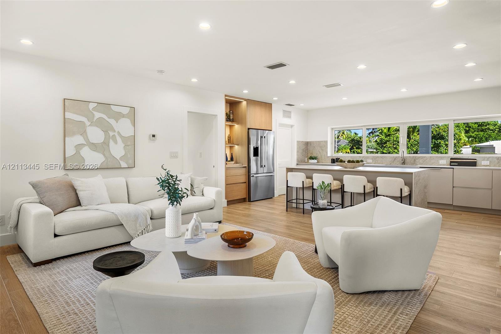 Open-concept kitchen featuring an expansive center island, integrated cabinetry, stainless steel appliances, and wood-finish flooring illuminated by recessed lighting