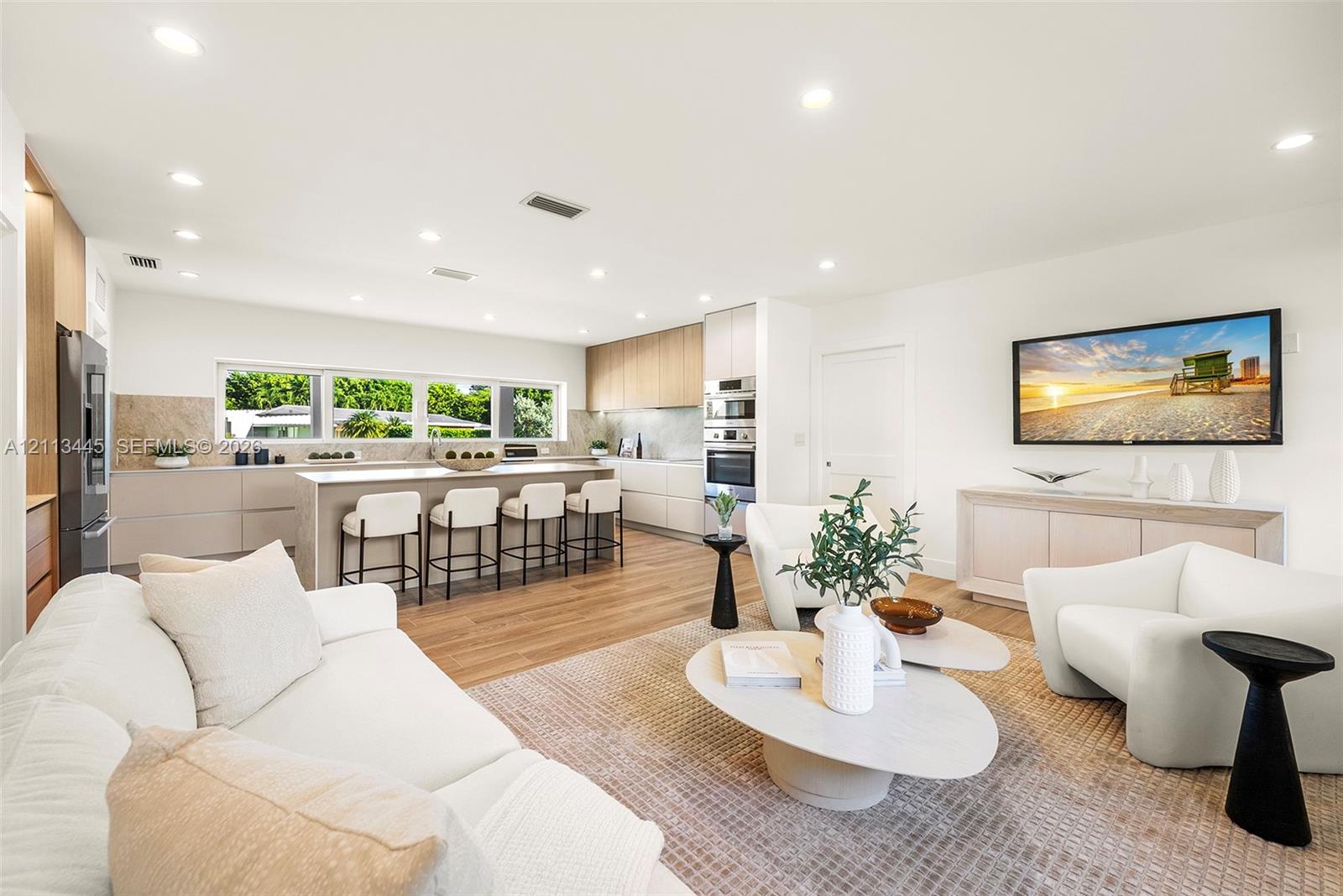 Open-concept living space featuring wood-finish flooring, recessed lighting, a central island with stone-finish countertops, handleless cabinetry, and built-in stainless steel appliances