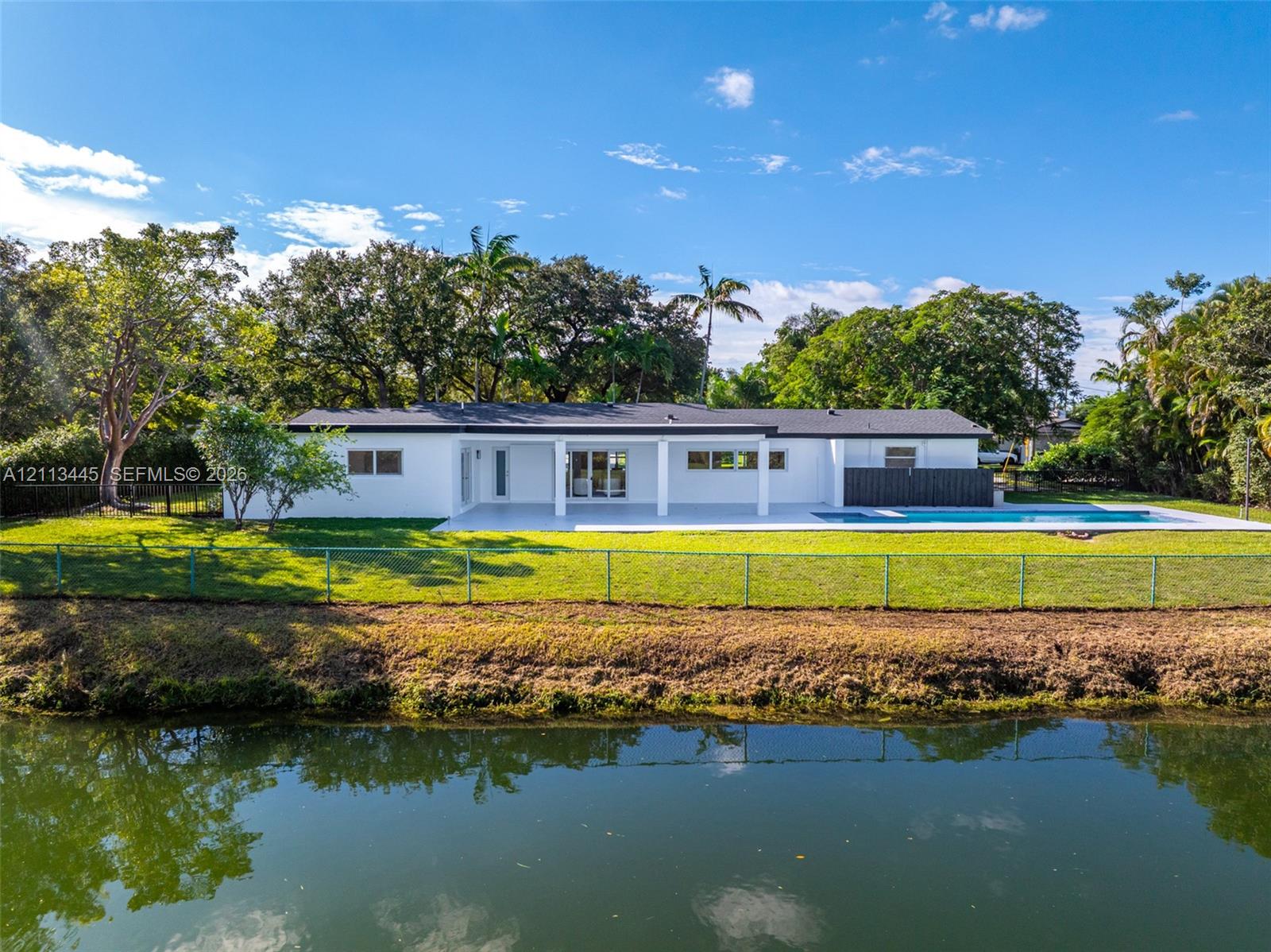Waterfront exterior featuring a covered patio, swimming pool, manicured lawn, and mature trees