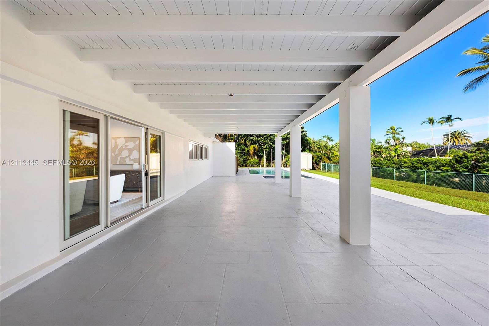Covered rear patio featuring a white-painted exposed beam ceiling, large-format tile flooring, and multiple sliding glass door entries