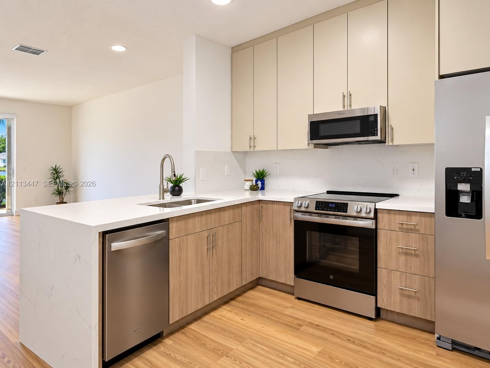 Kitchen featuring Carrara quartz countertops with waterfall edge, dual-toned cabinetry, and stainless steel appliances.