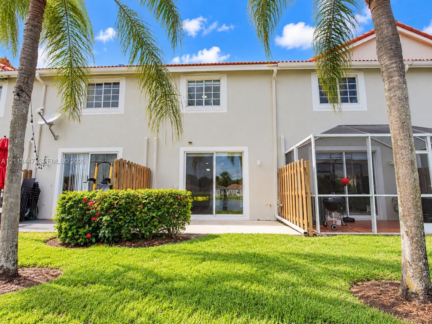 Stucco exterior featuring sliding glass doors, a screened-in patio, wooden privacy fencing, and a concrete slab