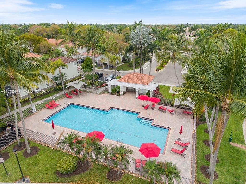 Swimming pool with paver decking, covered pavilion with clay-tile roof, and surrounding palm tree landscaping