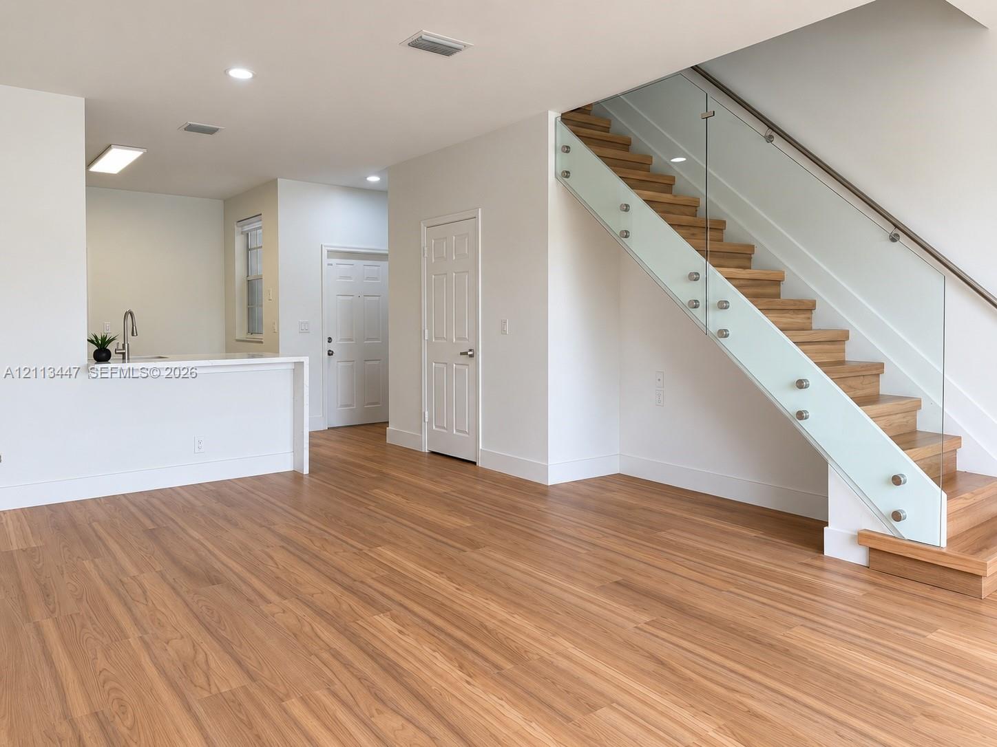 Open-concept interior featuring luxury laminated flooring, a staircase with glass panels and metal standoffs.