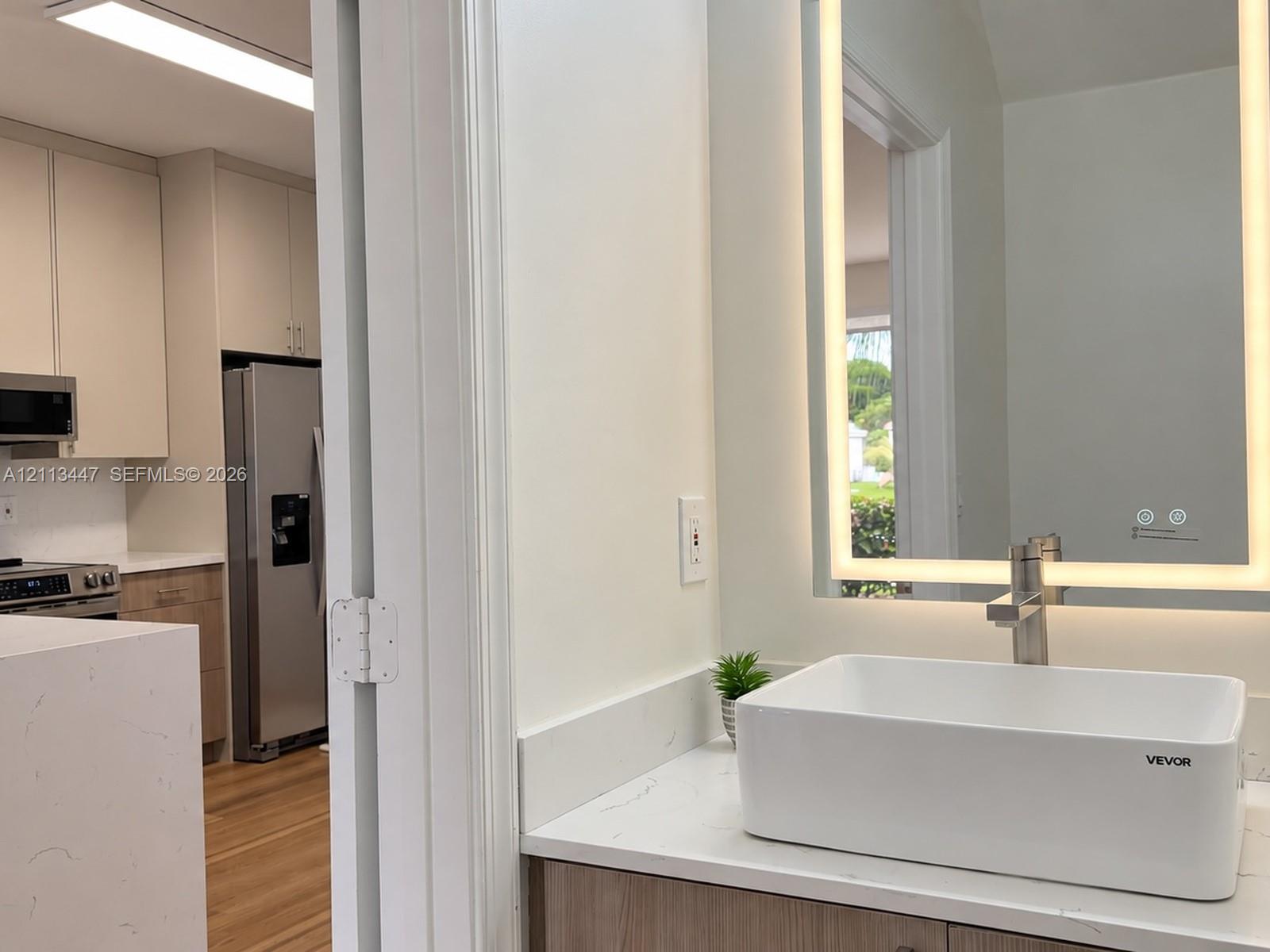 Bathroom vanity featuring a rectangular vessel sink, stone-finish countertop, wood-finish cabinetry, and an integrated LED-lighted mirror with stainless steel faucet