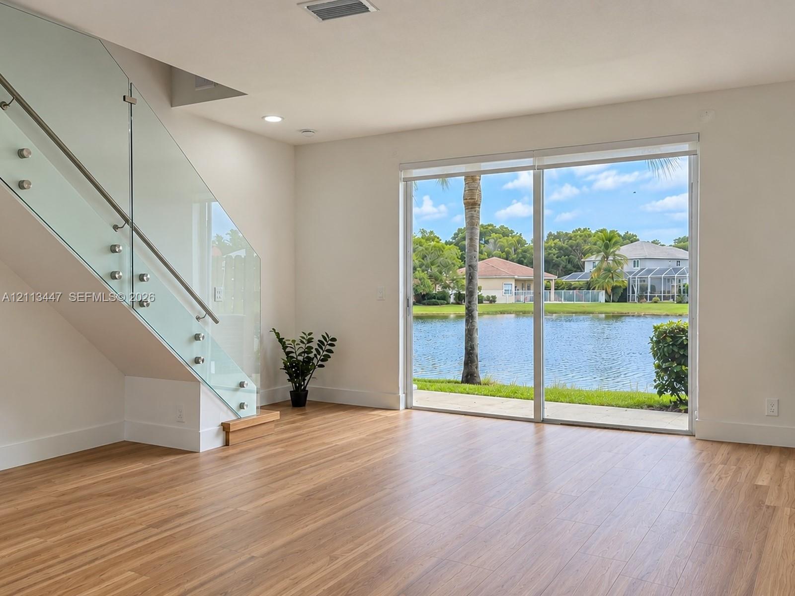 Staircase featuring a glass railing with stainless steel standoffs, luxury laminate flooring, and expansive sliding glass doors...