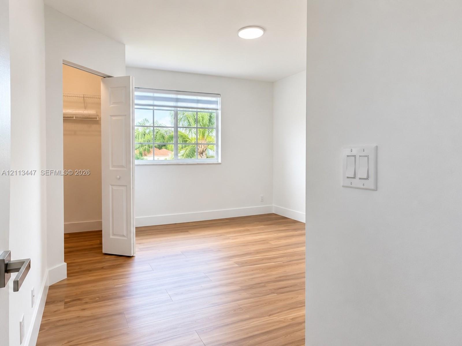 Room featuring wood-finish flooring, a multi-pane window, flush-mount lighting, and a closet with built-in shelving