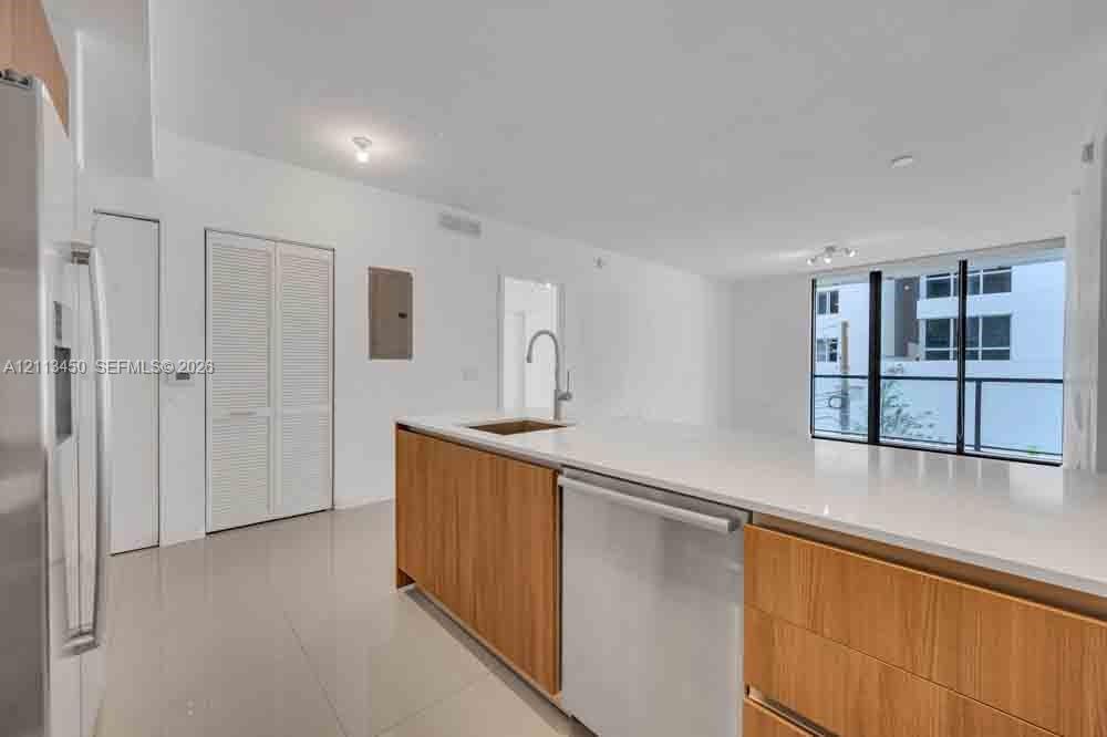 Kitchen featuring a quartz-topped island, light wood-finish cabinetry, stainless steel dishwasher, undermount sink with a gooseneck faucet, and polished tile flooring