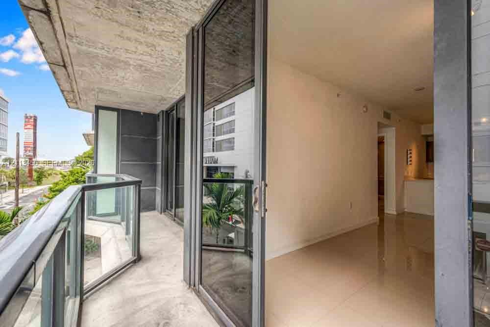 Covered private balcony featuring concrete ceiling, glass panel railing, sliding floor-to-ceiling glass doors, and polished tile flooring