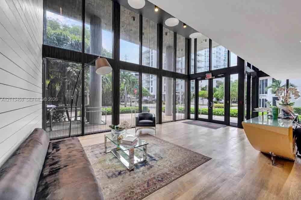 Double-height floor-to-ceiling windows, wood-finish flooring, horizontal shiplap wall paneling, and recessed ceiling lighting