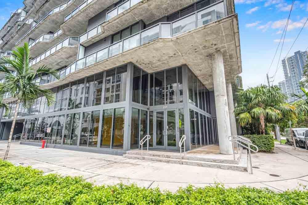 Contemporary multi-story exterior featuring floor-to-ceiling glass paneling, exposed concrete soffits, wrap-around glass balconies, and structural column supports