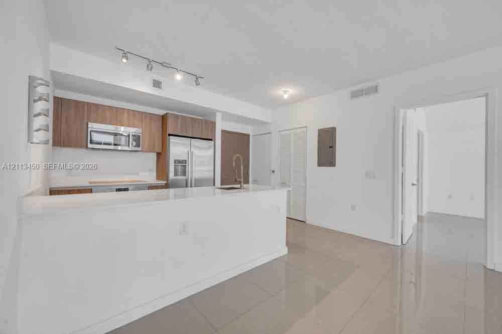 Kitchen featuring wood-finish cabinetry, white countertop, stainless steel appliances, track lighting, and tile flooring