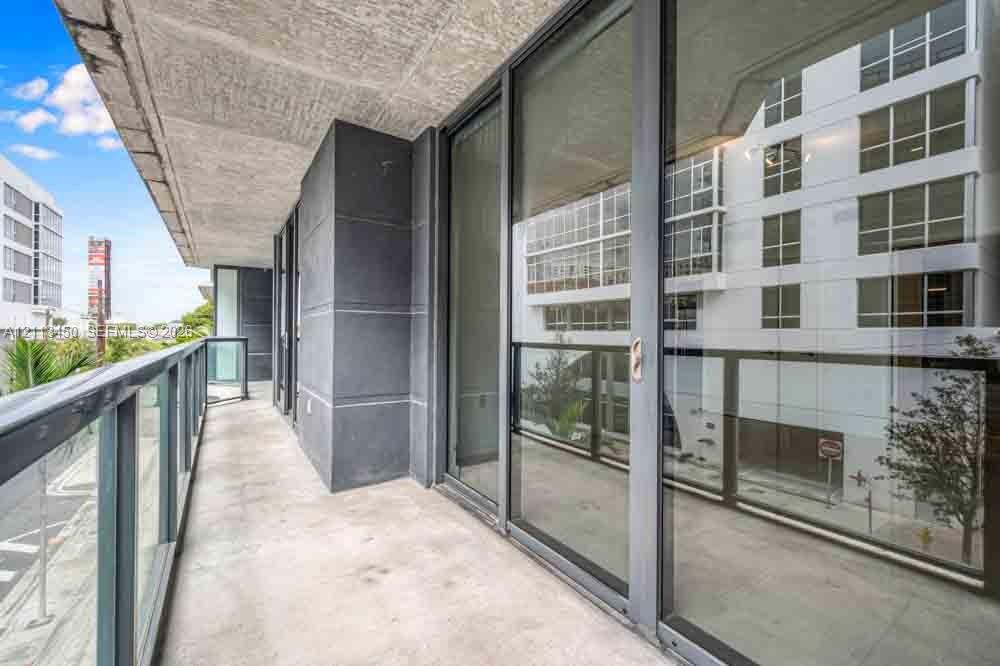 Covered private balcony featuring concrete flooring, charcoal-toned structural columns, and a glass-paneled railing system with full-height sliding glass doors