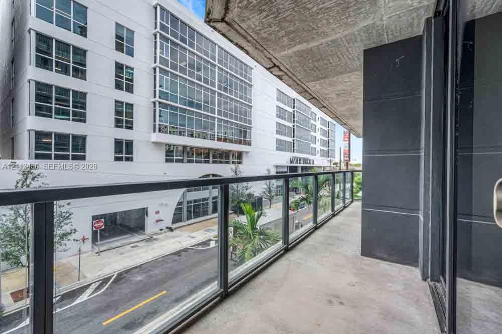 Covered balcony featuring concrete flooring, charcoal-toned vertical wall cladding, and a frameless glass railing system