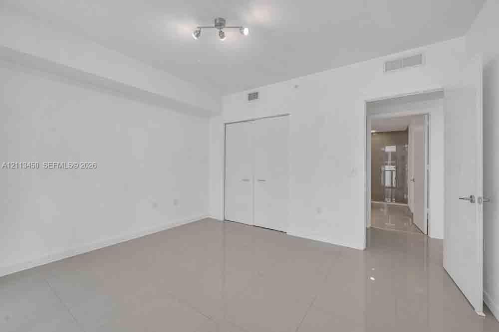 Neutral-toned tile flooring, recessed multi-directional lighting fixture, and white double-door closet cabinetry