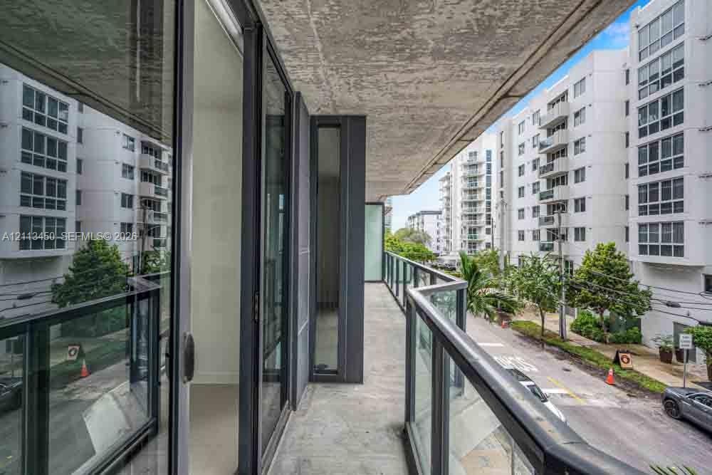 Covered outdoor balcony featuring a concrete floor, glass and metal railing, and floor-to-ceiling glass sliding doors