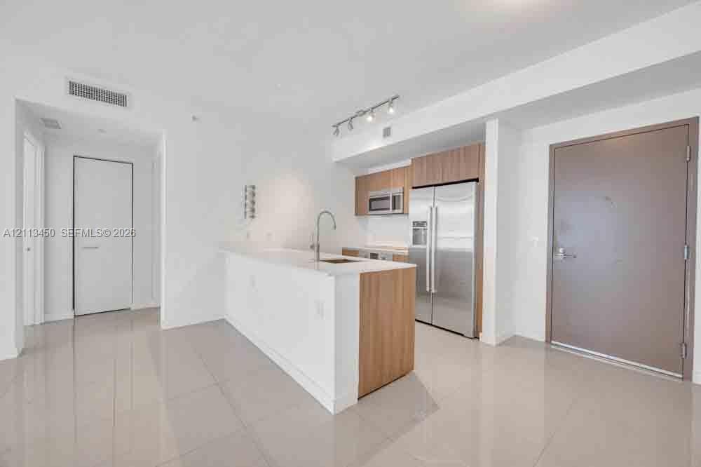 Kitchen featuring an island with a stone-finish countertop, wood-finish cabinetry, stainless steel appliances, and large-format tile flooring