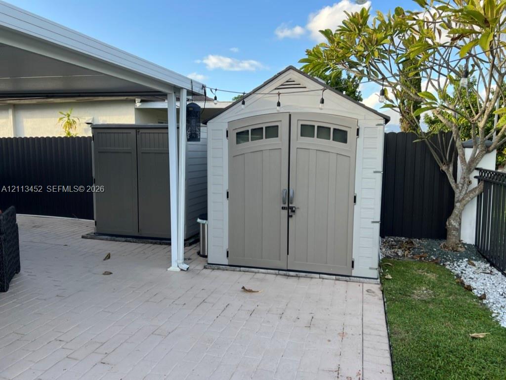 Exterior storage shed featuring dual entry doors, transom windows, and a neutral finish, situated on a paved patio surface