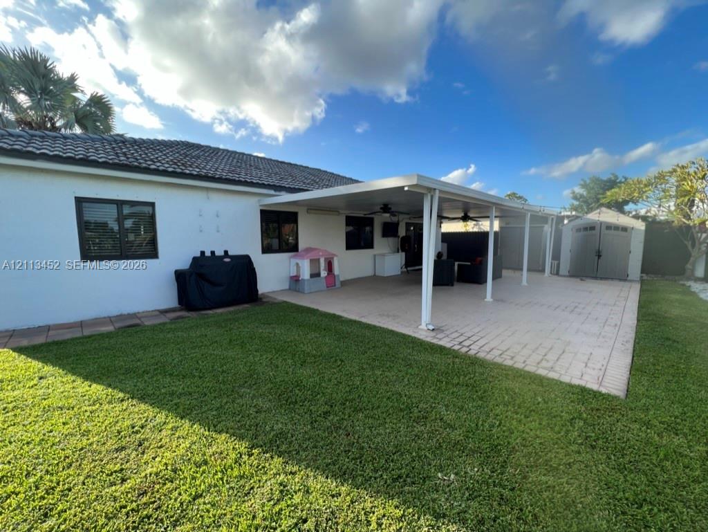 Backyard featuring a paved patio, a covered lanai with ceiling fans, and a detached storage shed