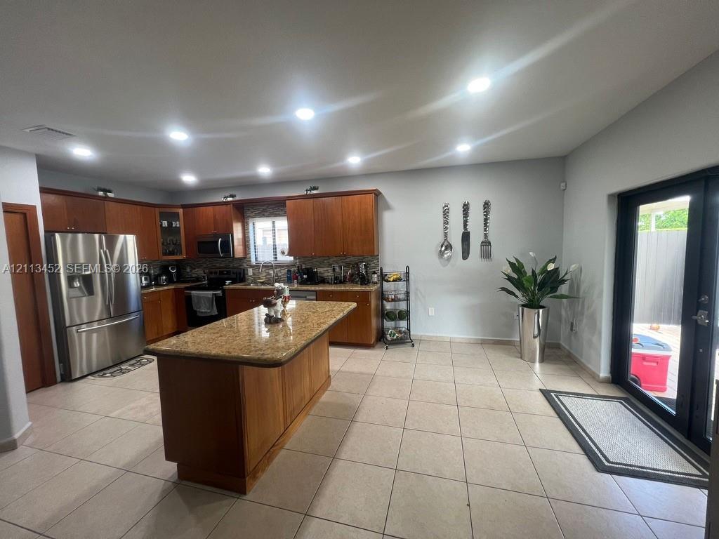Kitchen featuring wood cabinetry, a central island with stone-finish countertop, recessed lighting, tile flooring, and glass-paneled exterior door